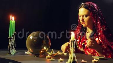 一个年轻的<strong>吉普</strong>赛人穿着红色的裙子在烛光下的桌子上读着石头上的未来。 平均计划